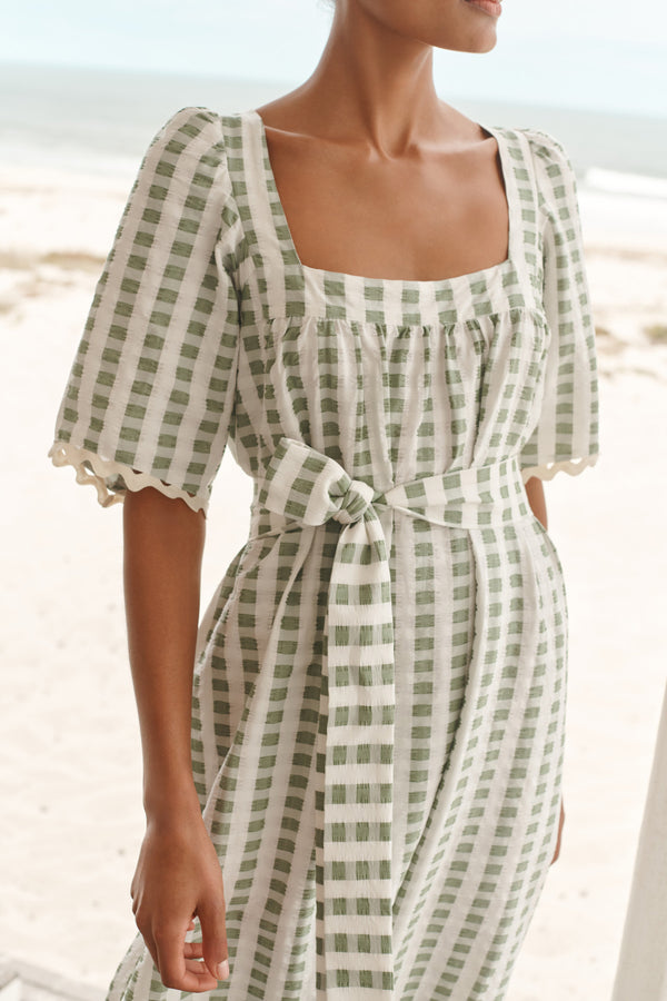 Wiggy Kit | Bastide Dress | Model wearing green and white gingham dress with beach in background